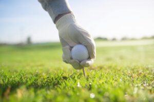 Close-up of a hand placing a golf ball on a tee in sunlight, outdoors.